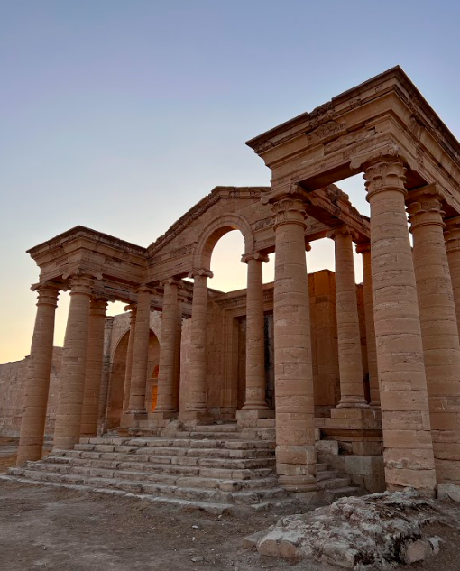 A grand, ancient Roman temple with towering columns and stone steps stands under a pale sky, bathed in soft light.