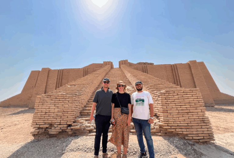 Three tourists pose in front of the ancient Ziggurat of Ur in Iraq under a bright sunny sky.