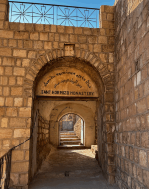 Mosul Day Tour from Erbil A stone archway with "Sant Hormizd Monastery" inscribed above, leads to a tunnel and stairs, offering a glimpse of the outside.