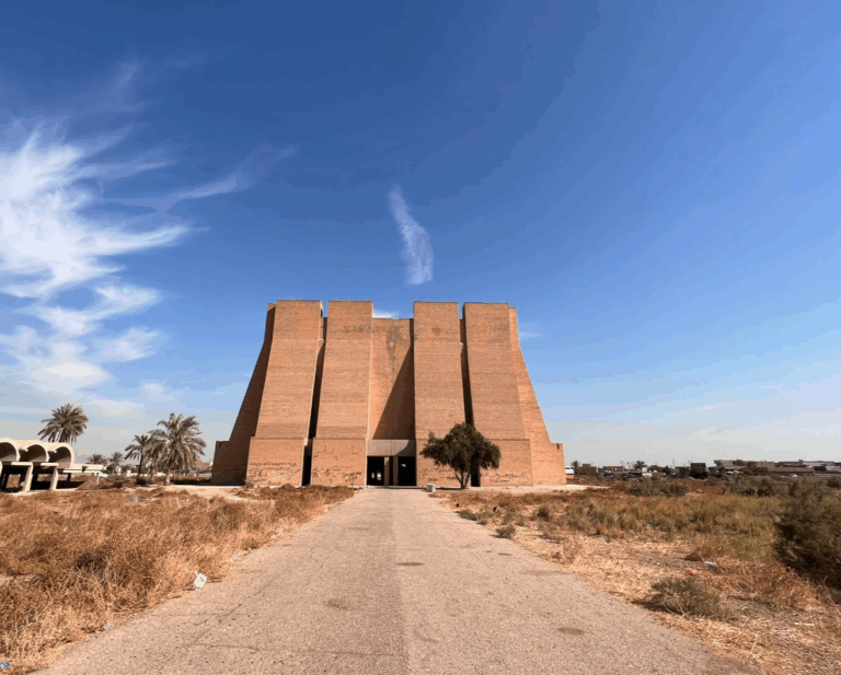 A wide shot of the Martyr Monument in Baghdad, Iraq, featuring its unique stepped brick facade under a clear blue sky.