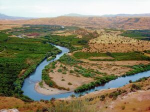 Day Tour Erbil A winding river meanders through a lush green valley surrounded by arid hills and mountains.