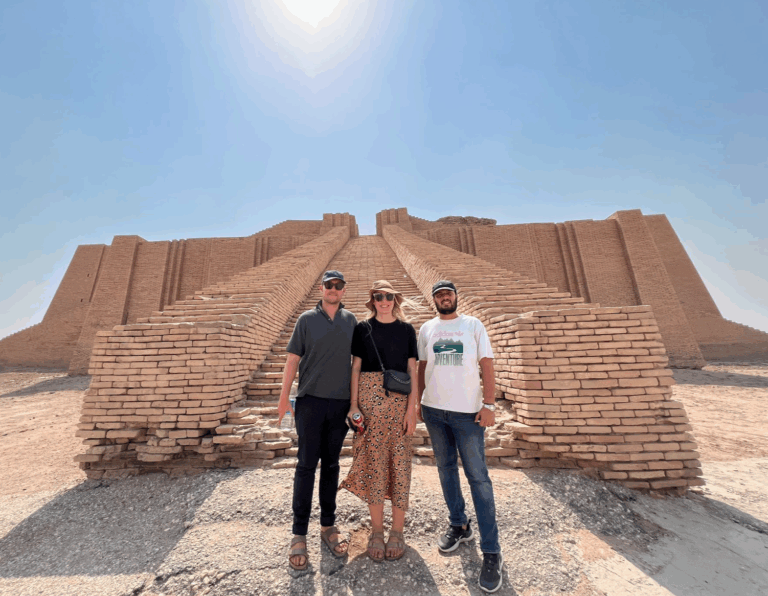Three people stand smiling in front of the ancient Ziggurat of Ur under a bright, sunny sky.
