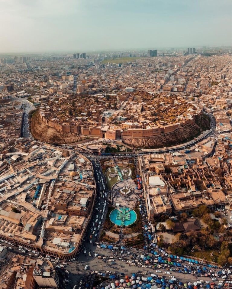 An aerial view shows the ancient Citadel of Erbil in Iraq, surrounded by a dense cityscape and bustling streets.