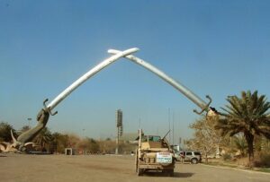 Day Tour Baghdad A military vehicle is positioned under a monument featuring two crossed swords held by large hands in Iraq.